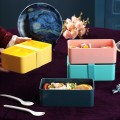 Lonchera tipo bento box con cierre elástico y compartimentos internos. Incluye cubiertos y está disponible en varios colores elegantes VENTA AL POR MAYOR 475LU