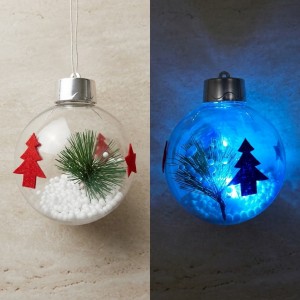 Esfera navideña transparente de 8 cm con luz LED y decoración interior, ideal para adornar árboles y espacios festivos. Venta por mayoreo